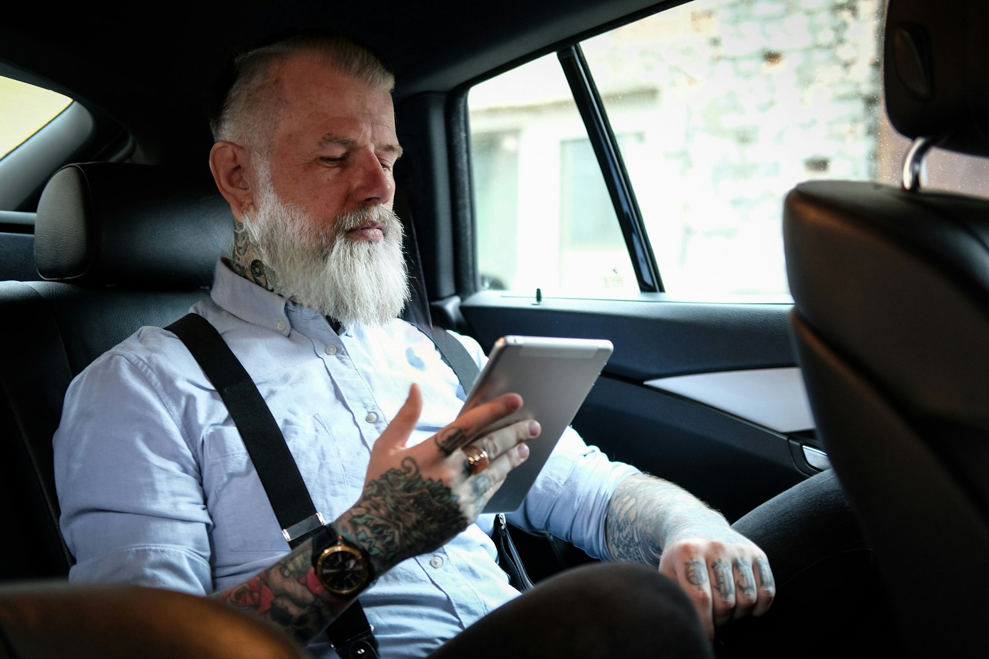 Old man businessman with tablet inside car in daytime